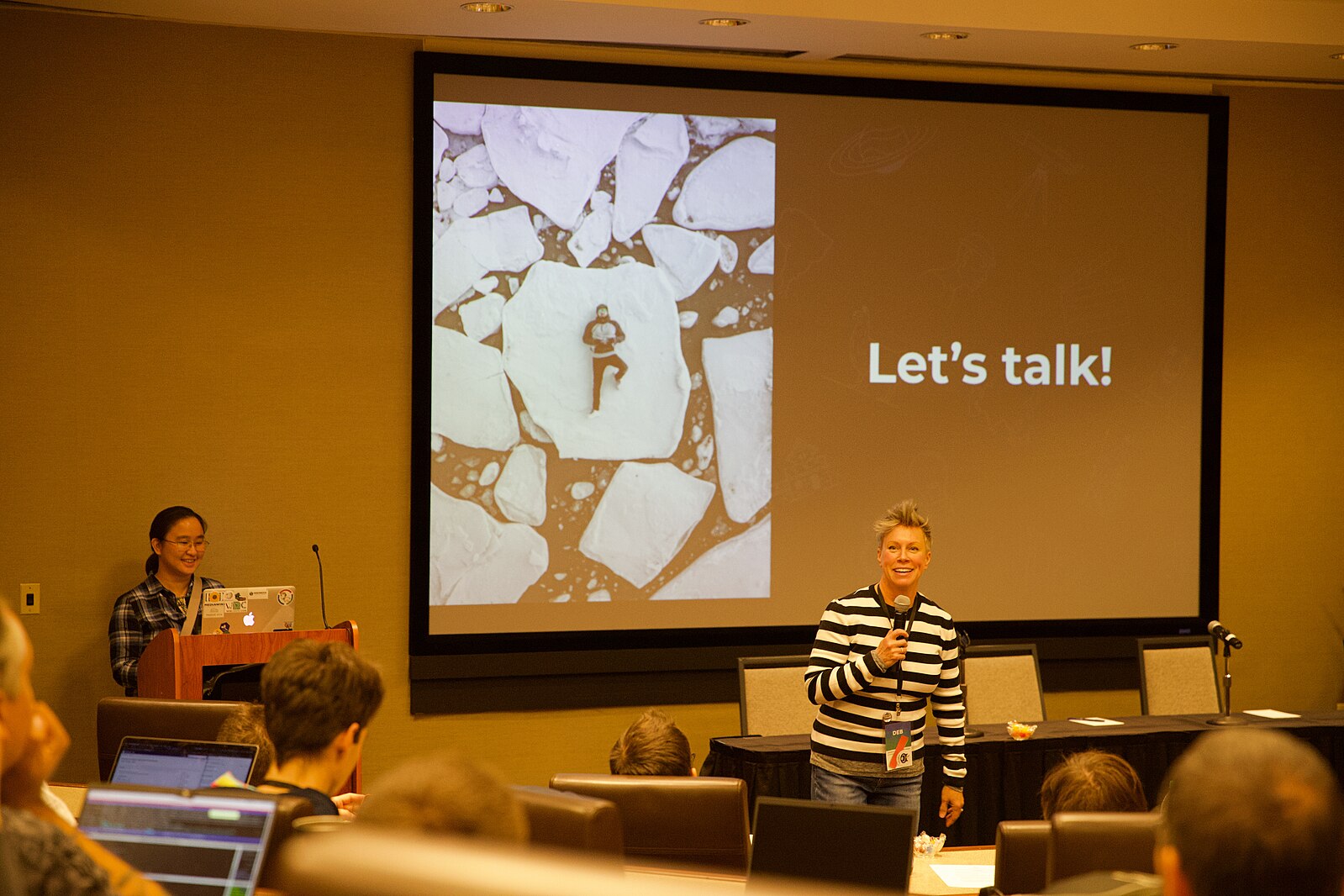 Person standing with a microphone in front of a screen showing the words “let’s talk”